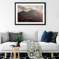 a framed fine art photograph of A dramatic view of the eastern edge of The MacGillycuddy's Reeks, Ireland's highest mountain range with the peak of Cruach Mhor visible against a bright cloudy sky hanging on a whit wall above a white sofa in a living room