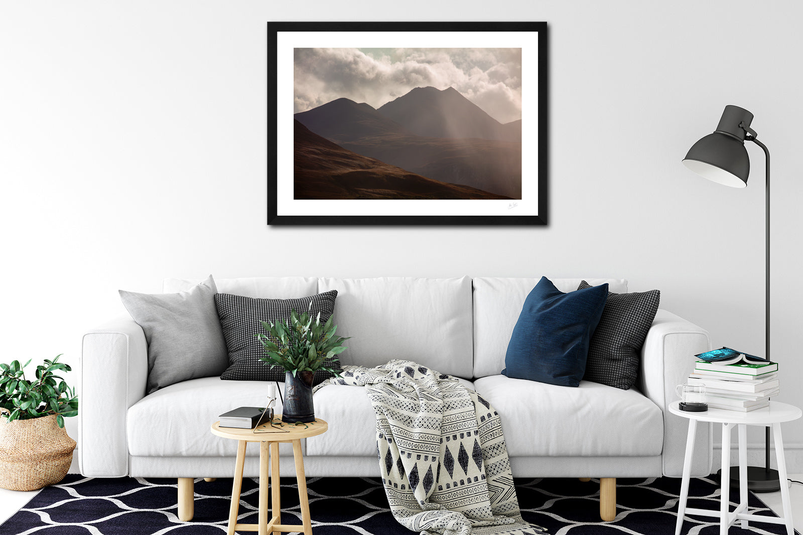 a framed fine art photograph of A dramatic view of the eastern edge of The MacGillycuddy's Reeks, Ireland's highest mountain range with the peak of Cruach Mhor visible against a bright cloudy sky hanging on a whit wall above a white sofa in a living room