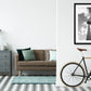 framed print of Berlin's TV tower from below touching the clouds in the sky on a wall in a room with a sofa and bycicle