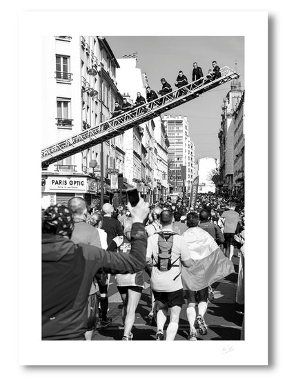 an unframed fine art photographic print of Parisian firemen sitting on a ladder above a Paris street during the Paris Marathon to support the runners, available to buy online