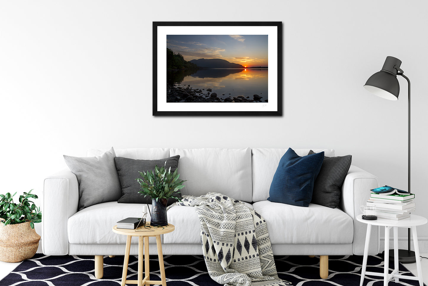 a framed fine art photographic print of the summer sun setting behind Shehy mountain across a calm Muckross Lake in Killarney National Park, hanging on a wall above a sofa