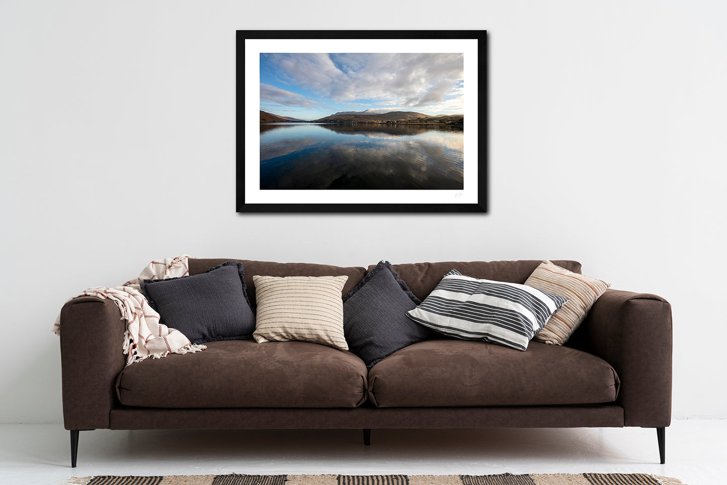 a framed fine art photographic print of Leenane village on Killary Fjord, Connemara on a calm winter's morning, hanging on a wall above a brown sofa